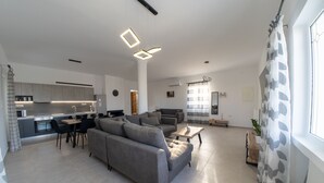 A modern living room with a grey sofa, a dining area, and a kitchen in the background. - Villa Nontas Ntina with Private Pool (Rethymno)