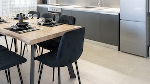 A modern kitchen with grey cabinets, a stainless steel refrigerator, and a dining area with a wooden table and black chairs. - Villa Nontas Ntina with Private Pool (Rethymno)