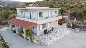 Une maison à deux étages dotée d’une terrasse, d’un espace salon extérieur et offrant une vue sur le paysage environnant.