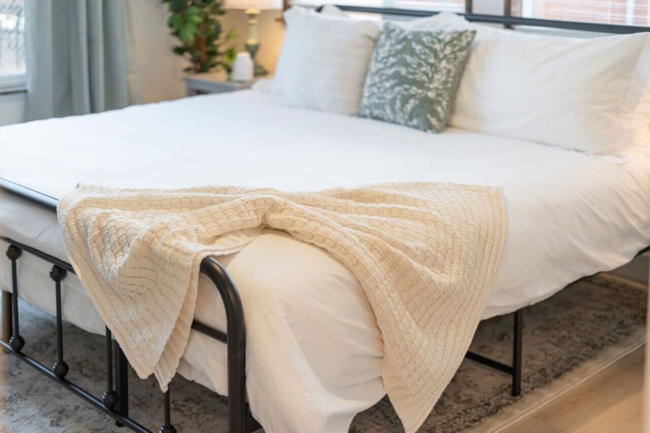 Een keurig opgemaakt bed met een witte deken en een beige gebreide plaid.