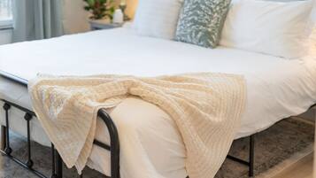 Een keurig opgemaakt bed met een witte deken en een beige gebreide plaid.