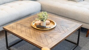 Et firkantet træbord med et geometrisk mønster, en bakke med en lille plante og en fjernbetjening.