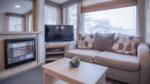Ein Wohnzimmer mit einer Couch, einem Flachbildfernseher, einem Kamin und einem Couchtisch mit einer Pflanze.