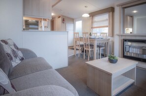 Un salon moderne avec un canapé, un coin repas avec des chaises, une cuisine avec une cuisinière et une petite table agrémentée d’une plante.