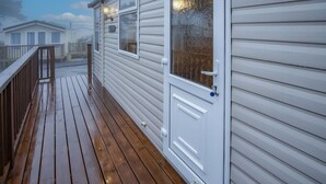 Eine Holzdielen-Terrasse mit einer weißen Tür und Fenstern, die zu einer überdachten Veranda führt.