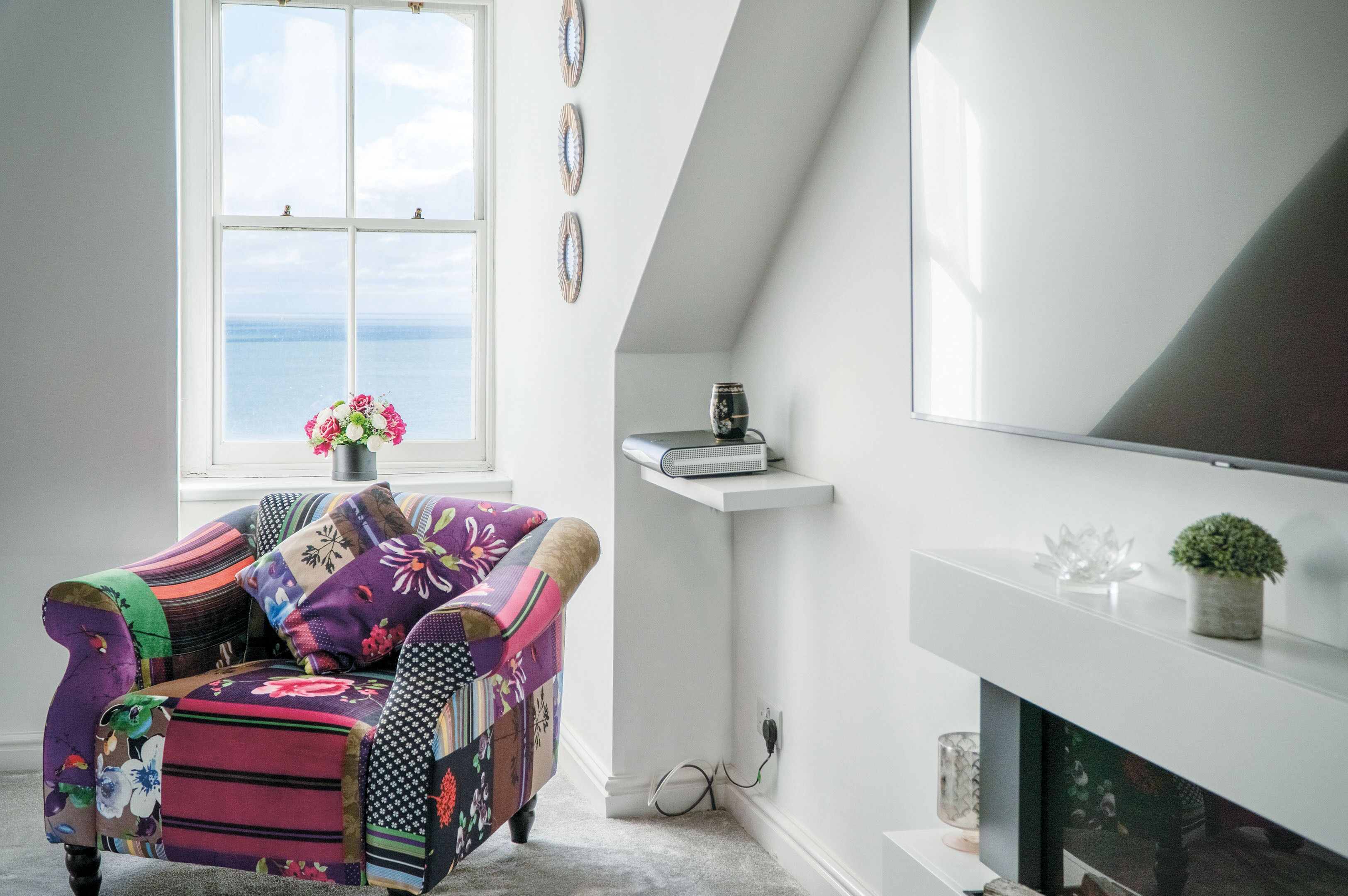 Una sala de estar acogedora con un sillón colorido, una chimenea y vistas al mar a través de un amplio ventanal.