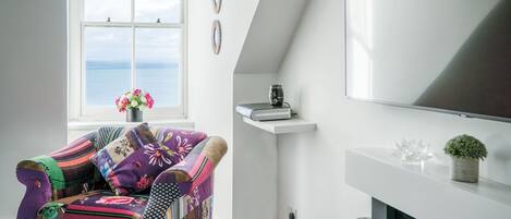 Una sala de estar acogedora con un sillón colorido, una chimenea y vistas al mar a través de un amplio ventanal.