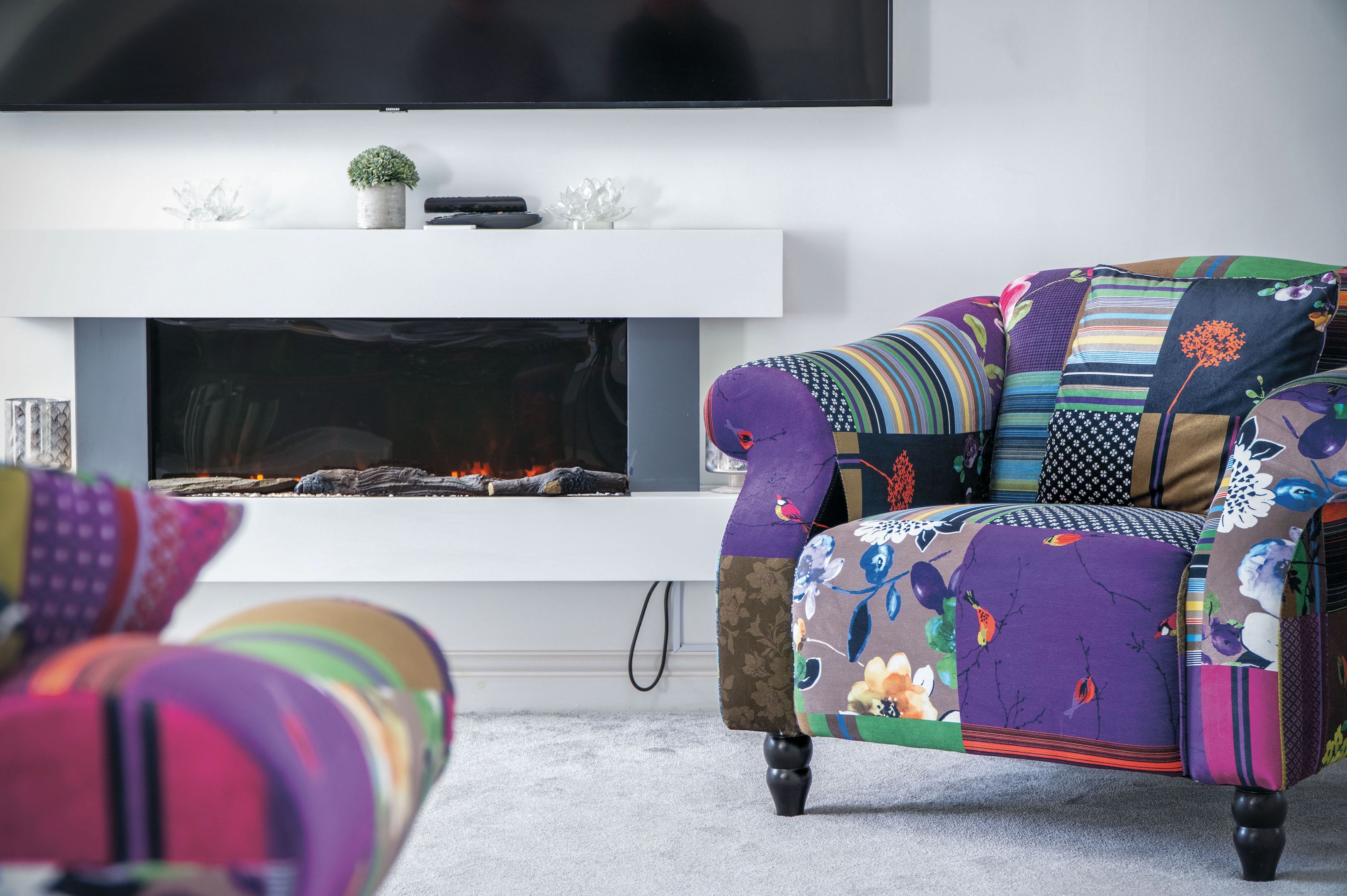 A modern living room with a fireplace, a colorful armchair, and a sofa with a floral pattern.