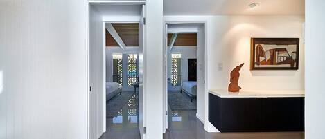 Un interior moderno con un pasillo que lleva a dos dormitorios, una chimenea y una escultura en la pared.