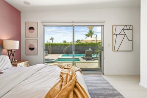 Un dormitorio con cama, mesita de noche, lámpara y vista a una piscina a través de una puerta corredera.