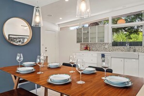 Un comedor con una mesa de madera dispuesta para seis personas, un espejo redondo e iluminación colgante.