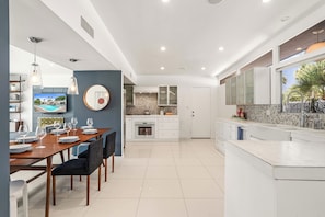 A modern kitchen with white cabinets, a tiled backsplash, and a dining area with a wooden table and chairs.