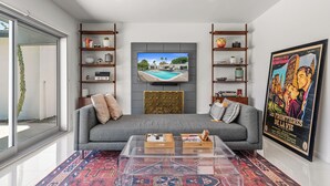 A modern living room with a grey sofa, a glass coffee table, and a TV mounted on the wall.