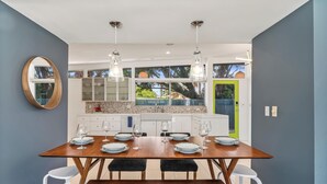 A modern kitchen with a dining table set for six, white chairs, and a large window with a view of greenery.
