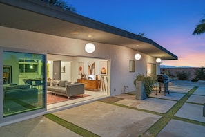 A modern house with a patio, a dining area, and a kitchen visible through glass doors.