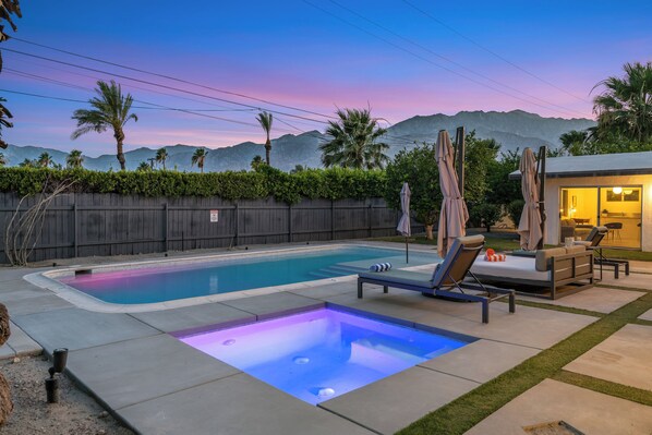Piscina con jacuzzi, sillas de descanso y una pequeña zona de patio.
