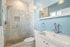 Un baño con ducha de mampara de vidrio, inodoro blanco, lavamanos con espejo y pared azul.