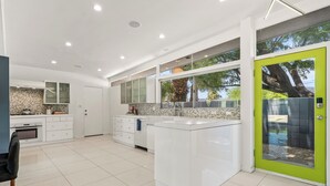 A modern kitchen with white cabinetry, a large island, and a green door.