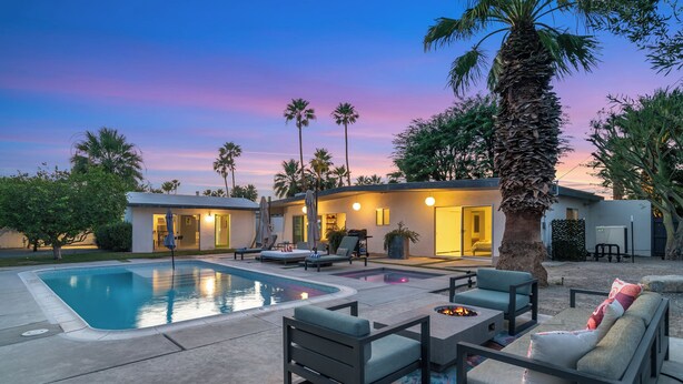 A pool area with lounge chairs, a fire pit, and a house with multiple doors and windows.
