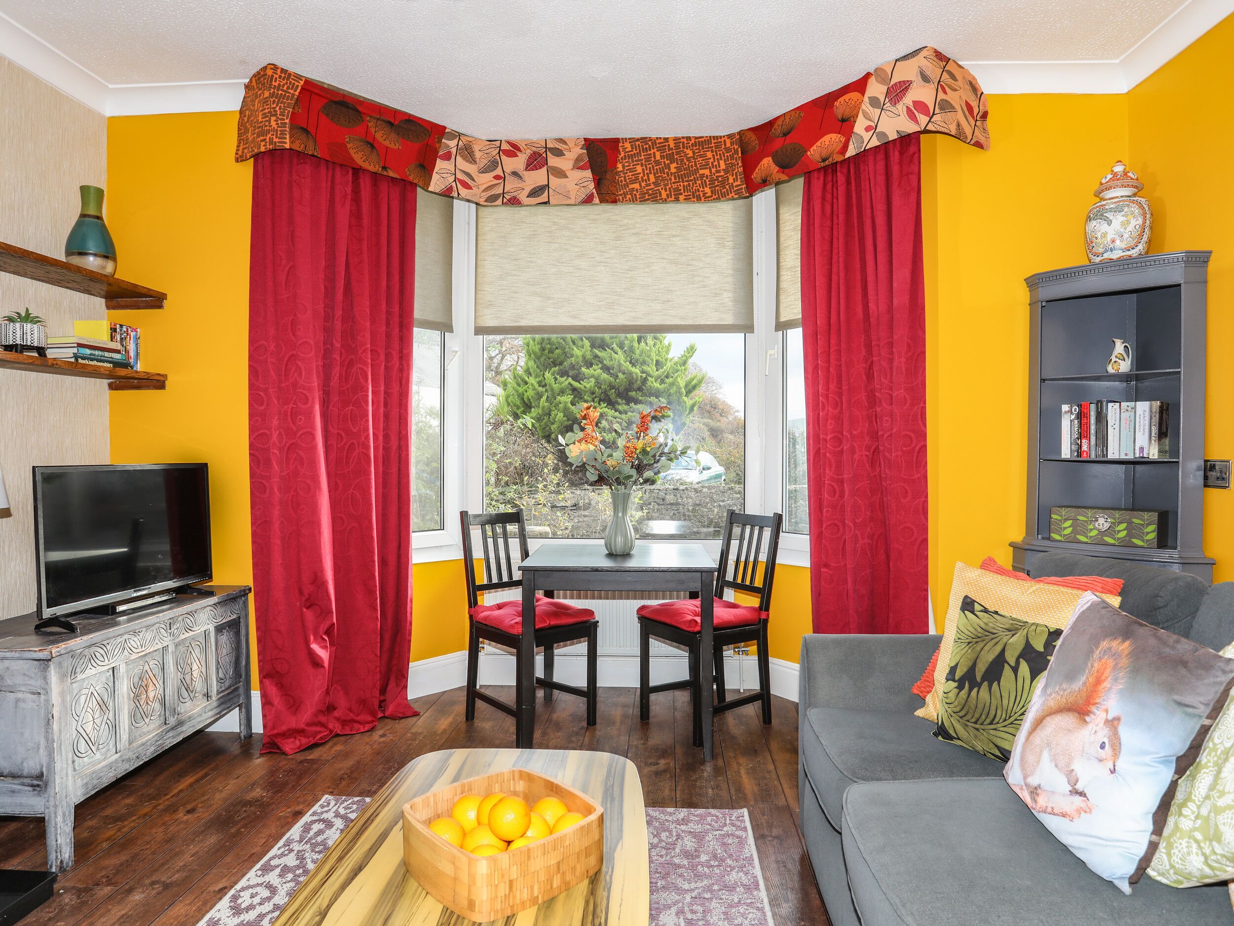 A living room with a TV, wooden table, chairs, a sofa, and a bookshelf.
