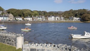 A harbor with several boats, a stone wall, and houses along the water's edge. - Gweldon - Anchor Deck (Porthmadog)