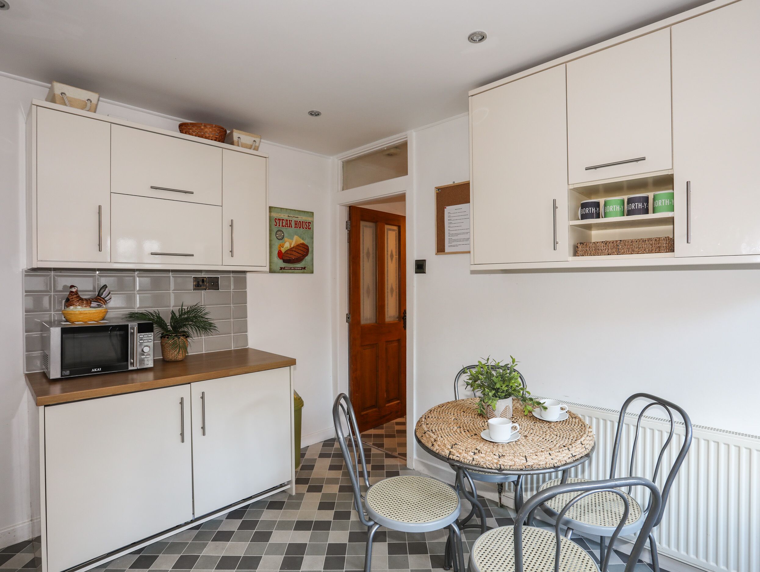 A compact kitchen with white cabinets, a microwave, and a small dining area with wicker chairs and a round table.