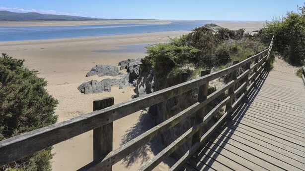 A wooden boardwalk leading to a beach with clear skies and distant mountains. - Gweldon - Anchor Deck (Porthmadog)