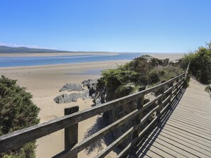 A wooden boardwalk leading to a beach with clear skies and distant mountains. - Gweldon - Anchor Deck (Porthmadog)
