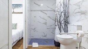 A bathroom with a shower, toilet, and a bed visible in the adjacent room. - AYZ Luis Cabrera-Auto check-in property (Madrid)
