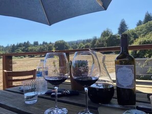 A table with two wine glasses, a bottle of wine, and a water bottle on an outdoor deck with a view of a forested landscape.