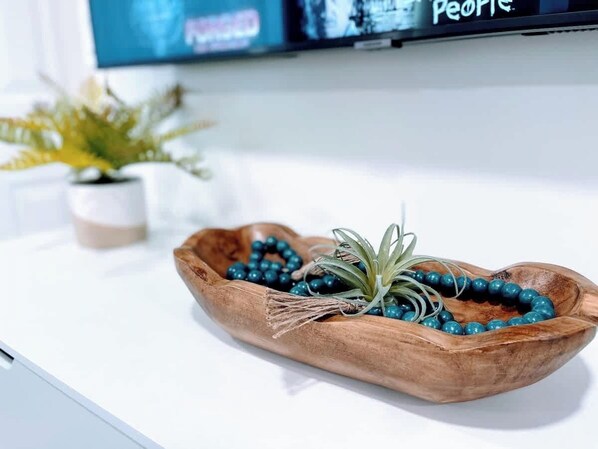 Un bol en bois orné de perles et une petite plante posés sur une surface blanche.
