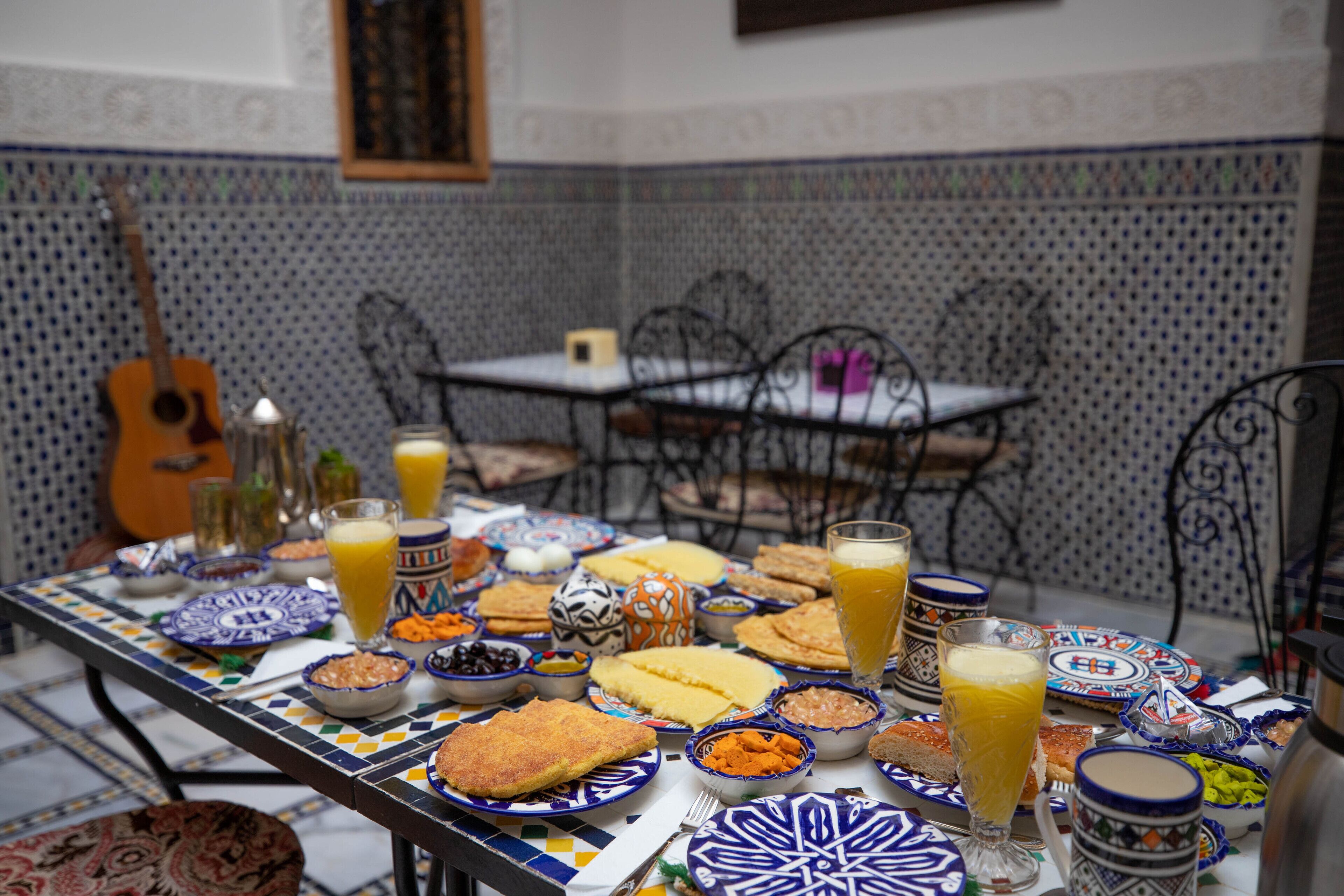 A dining table with various dishes and drinks, surrounded by patterned tiles and metal chairs.