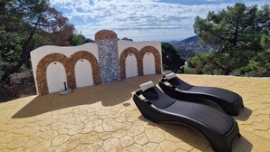 Jardín de sillones reclinables en un patio con baldosas, con una pared decorativa que incluye arcos de piedra y un panel de mosaico.