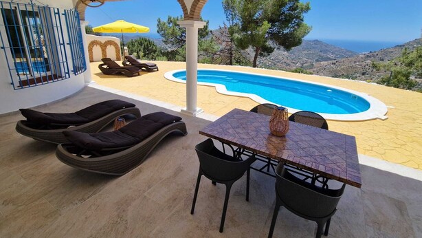 Zona junto a la piscina con sillones de descanso, una mesa y vista al mar.