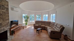 Un salón espacioso con chimenea de piedra, un sofá modular grande y un televisor de pantalla plana.