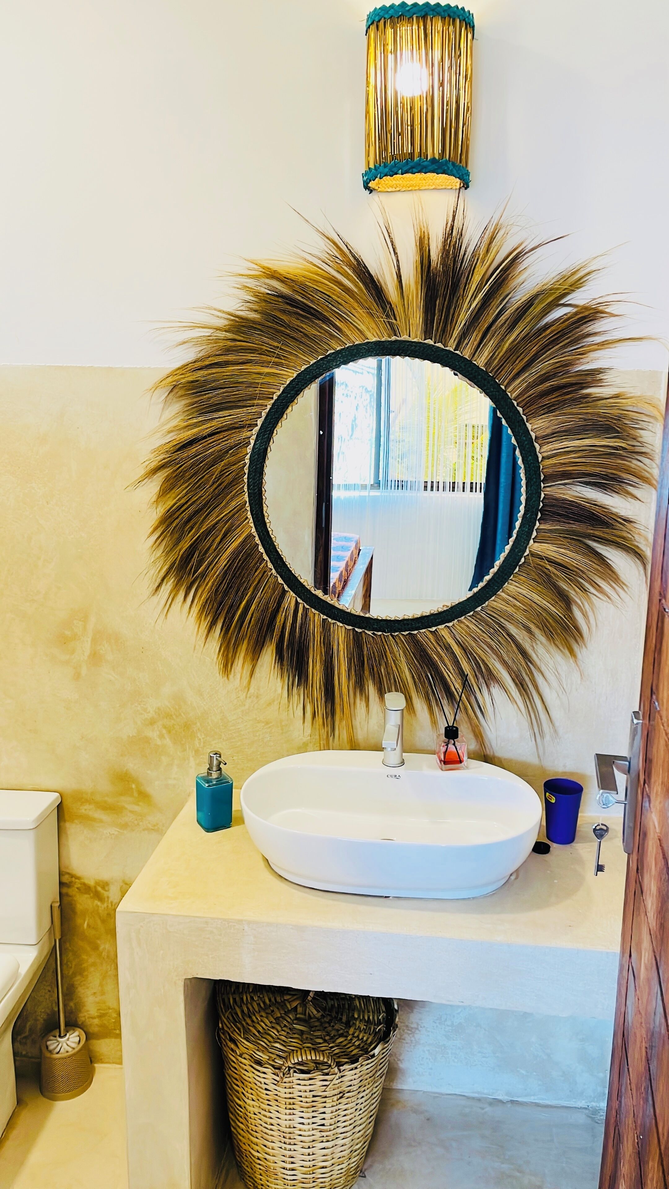 A bathroom with a round mirror, a white sink, a blue soap dispenser, and a decorative wall hanging.