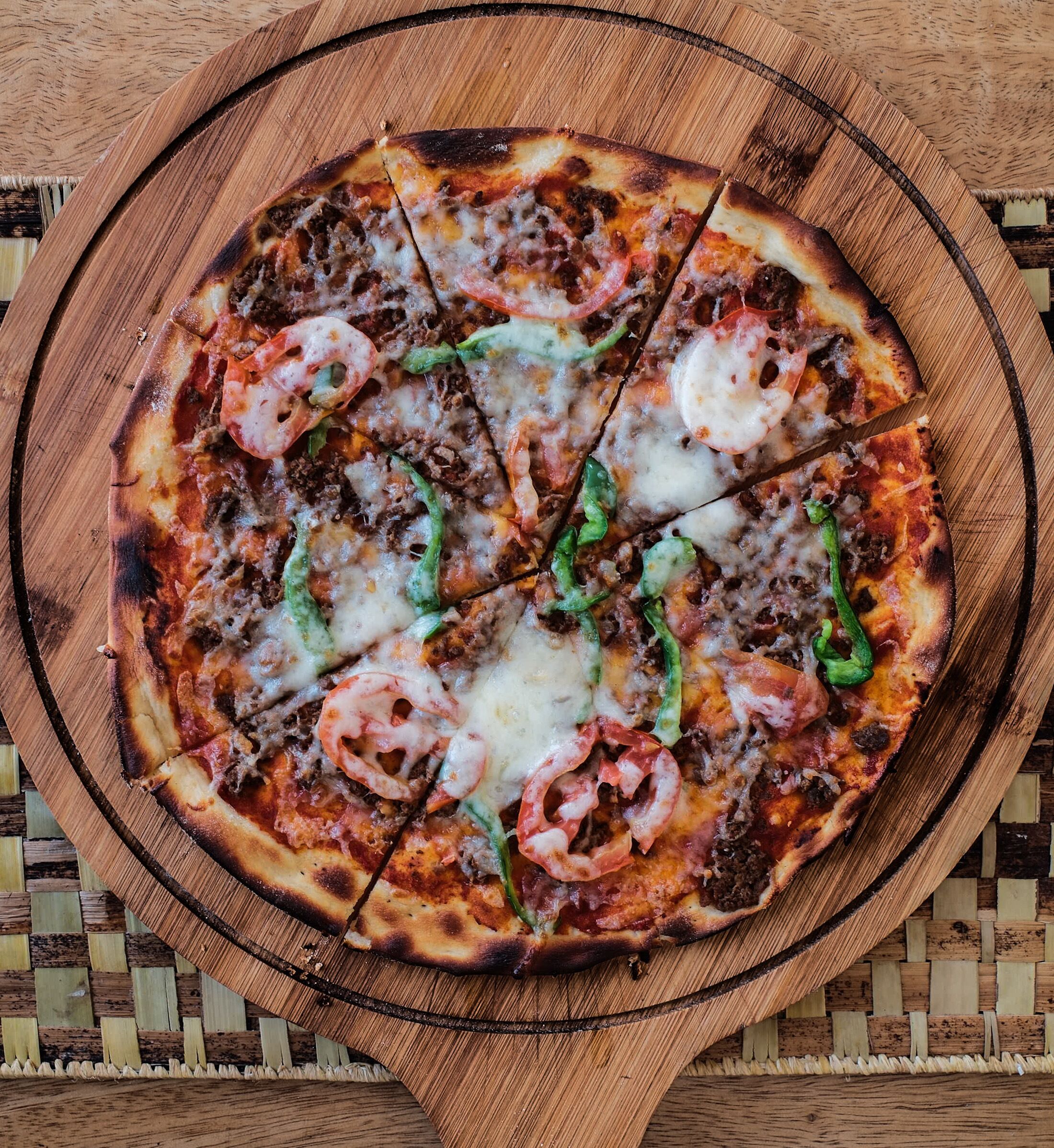 Pizza met diverse toppings op een houten plank.