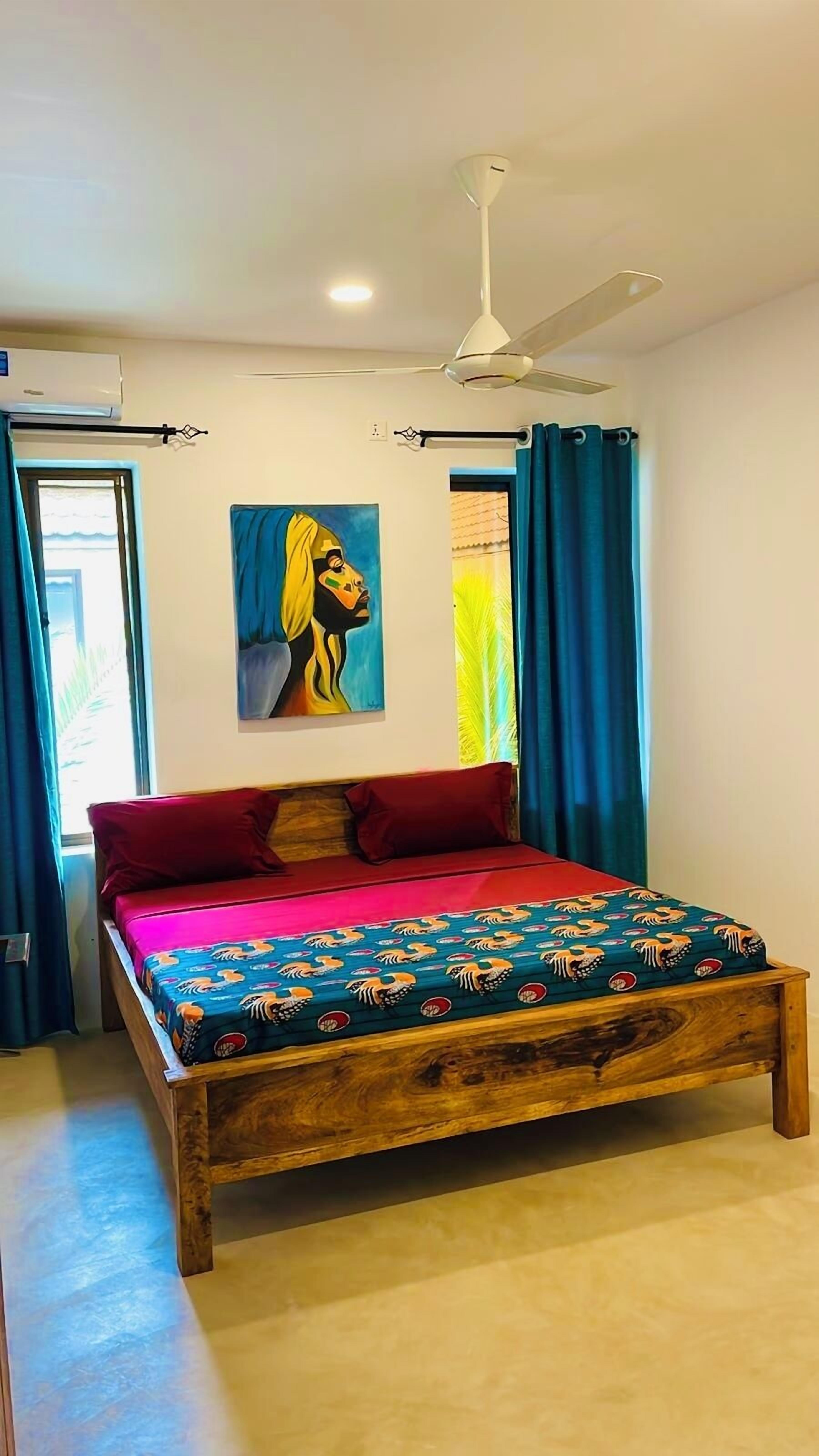 Un dormitorio con cama de madera, almohadas rojas, un ventilador de techo y un cuadro en la pared.