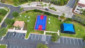 Vista aérea de una cancha deportiva con aro de baloncesto, una tienda de campaña azul y un estacionamiento con espacios delimitados.