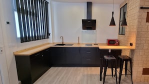 A modern kitchen with black cabinets, a wooden countertop, a red microwave, and black bar stools. - Loft Vintage (Santander)
