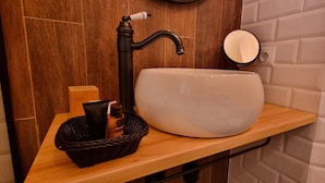 A bathroom with a wooden vanity, a large white sink, a black faucet, and a small round mirror. - Loft Vintage (Santander)
