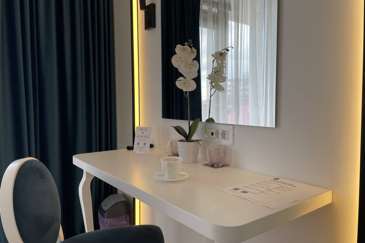 A hotel room with a white desk, a cup of coffee, a potted orchid, and a Wi-Fi sign.