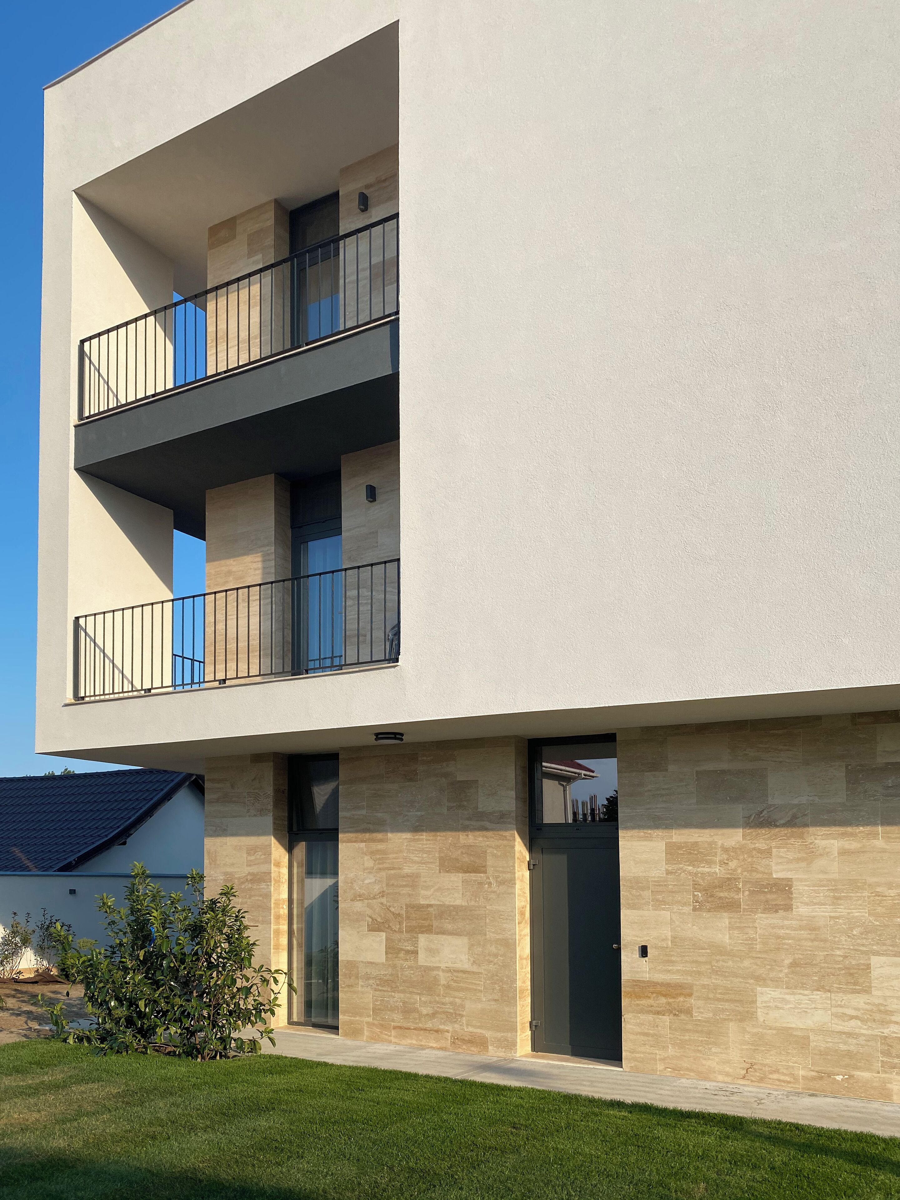Un edificio moderno de dos pisos con techo plano, ventanas grandes y un balcón con barandillas de metal.