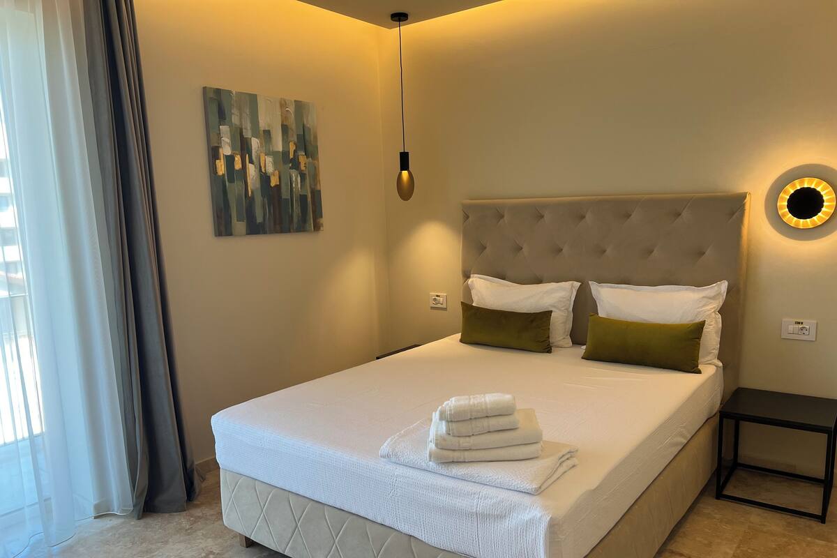 A neatly made bed with a quilted headboard, a bedside table, and a wall-mounted light fixture.