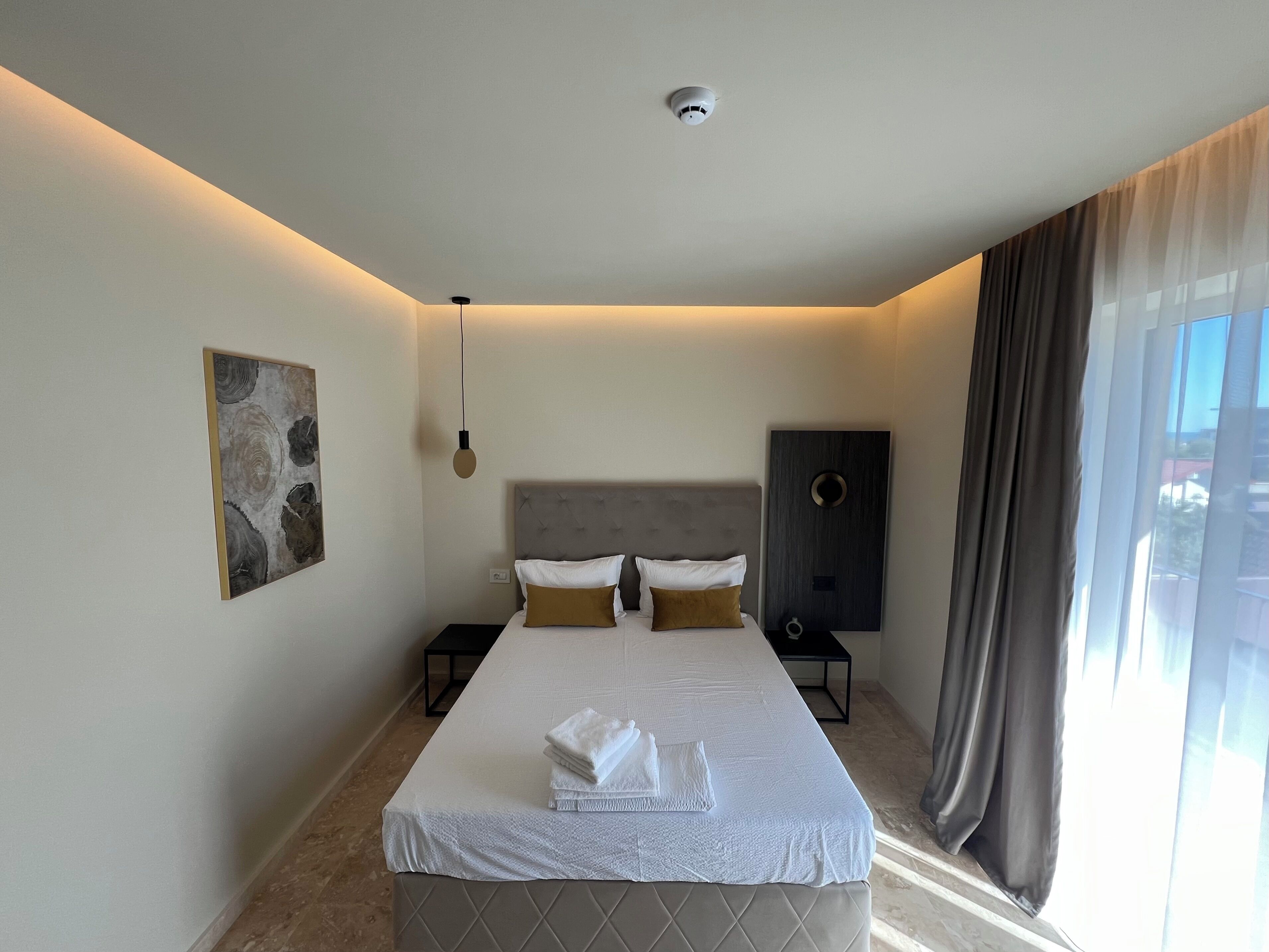 Una habitación de hotel moderna con una cama grande, un cabecero de diseño circular, una obra de arte en la pared, una mesita de noche y una ventana con cortinas.