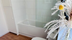 Une salle de bain avec des toilettes blanches, une baignoire et un plancher en bois.