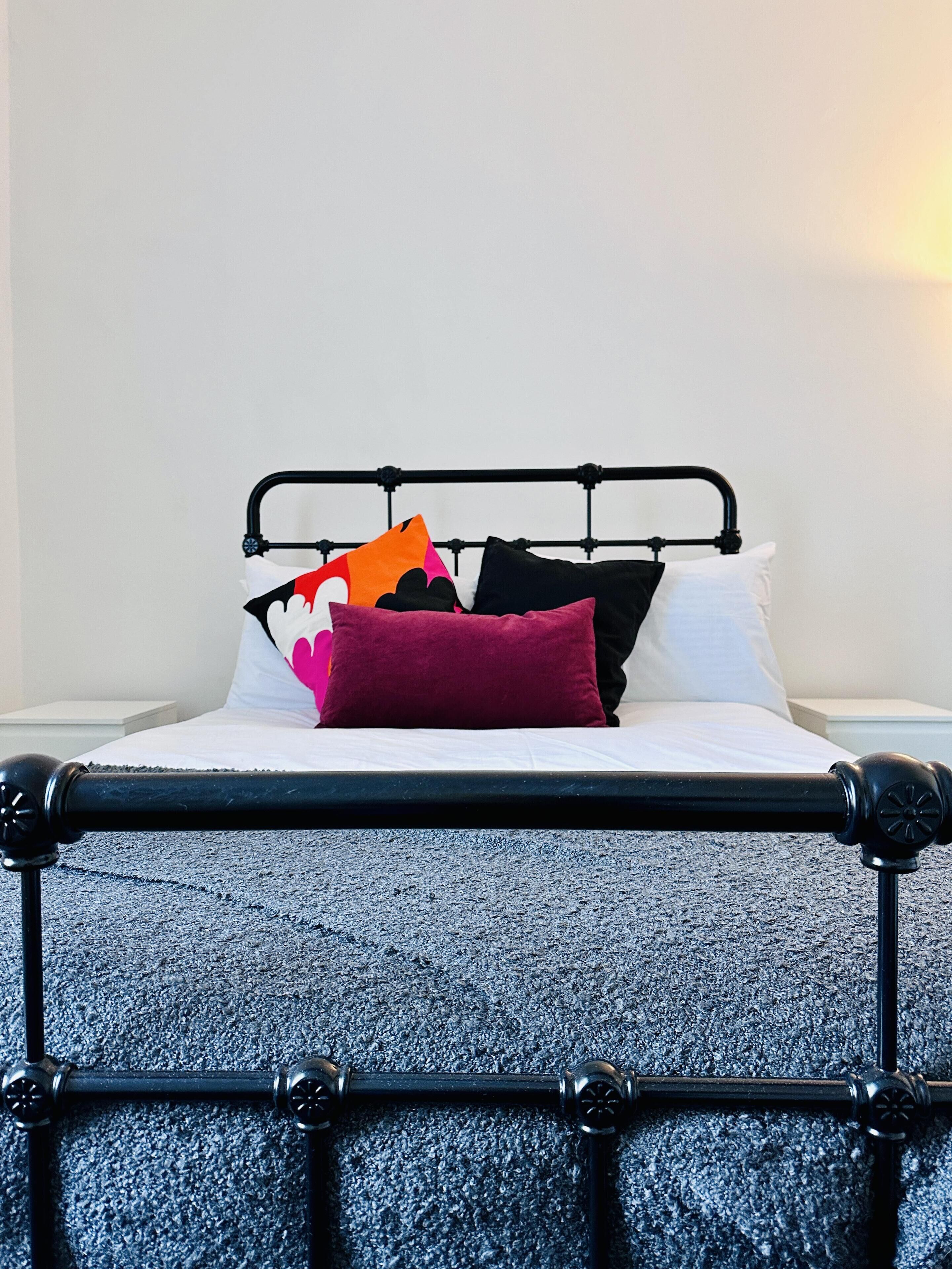 A bed with a black metal frame, white bedding, and multiple pillows in various colors.
