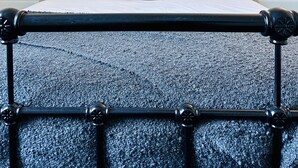 Un lit avec un cadre en métal noir, une literie blanche et plusieurs oreillers de différentes couleurs.