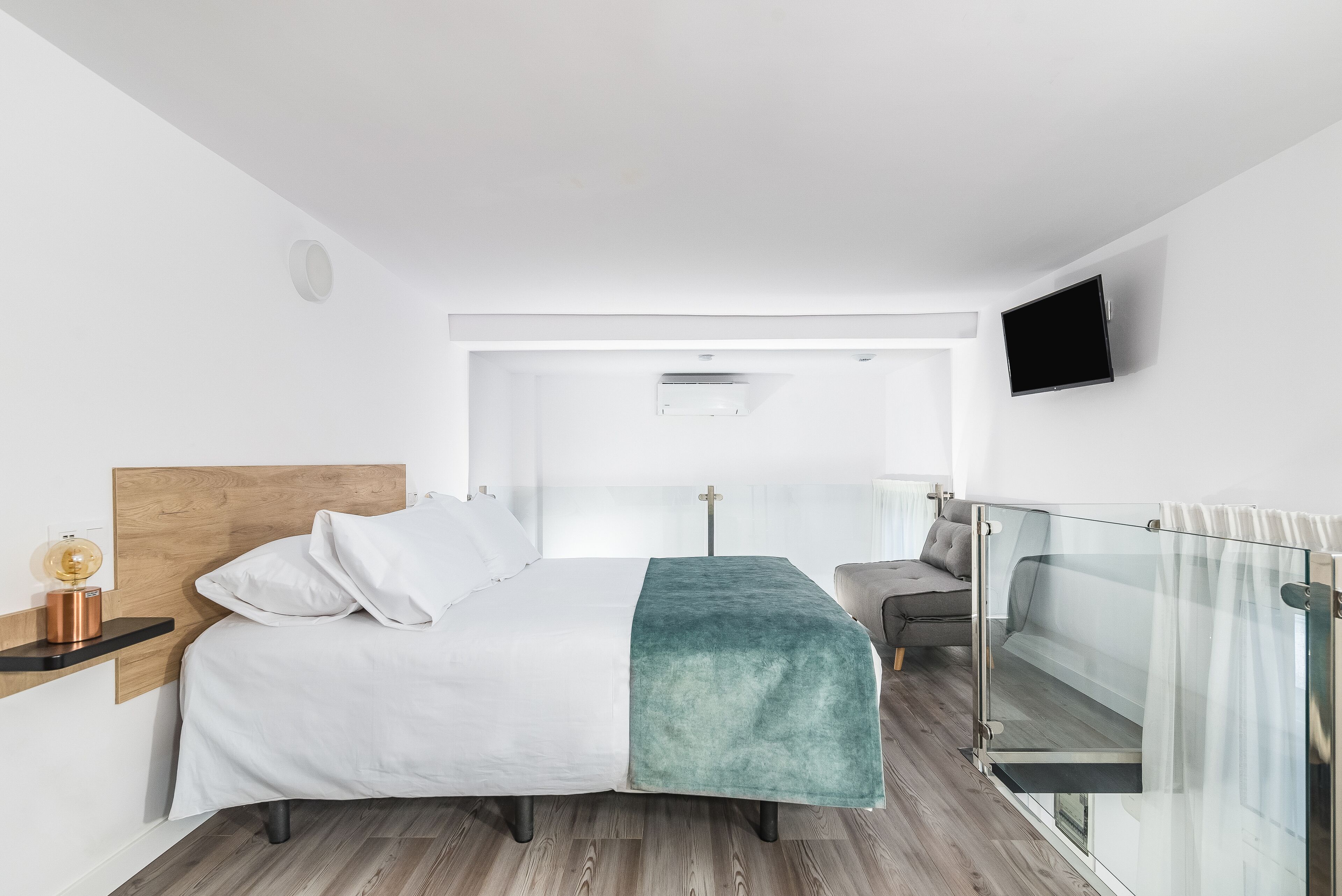 A modern hotel room with a bed, bedside table, lamp, and a view of the balcony.