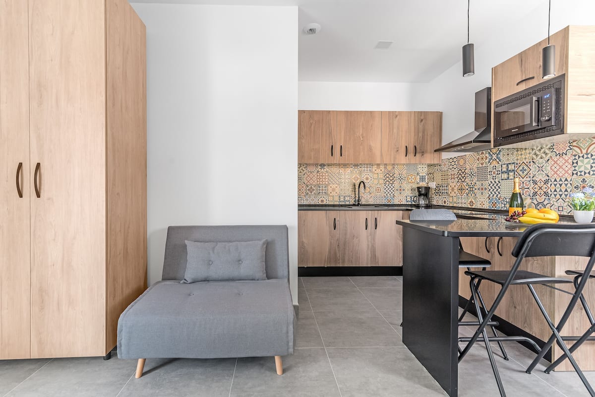 Una cocina moderna con armarios de madera, un sofá gris y una zona de comedor con una silla negra.